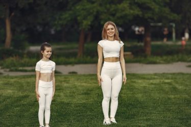 A woman and girl in white activewear standing on a grass field outdoors, smiling.