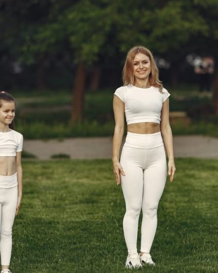 A woman and girl in white activewear standing on a grass field outdoors, smiling.