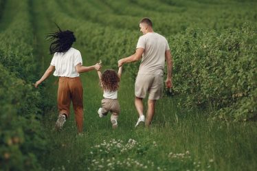 A joyful family strolls through a lush green field, enjoying quality time together.