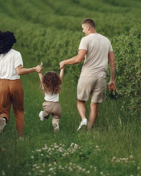 A joyful family strolls through a lush green field, enjoying quality time together.