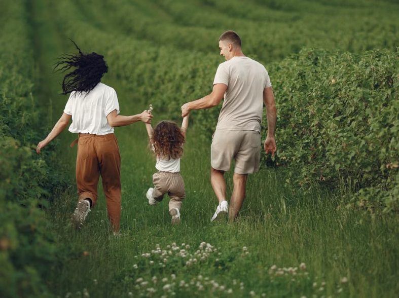 A joyful family strolls through a lush green field, enjoying quality time together.